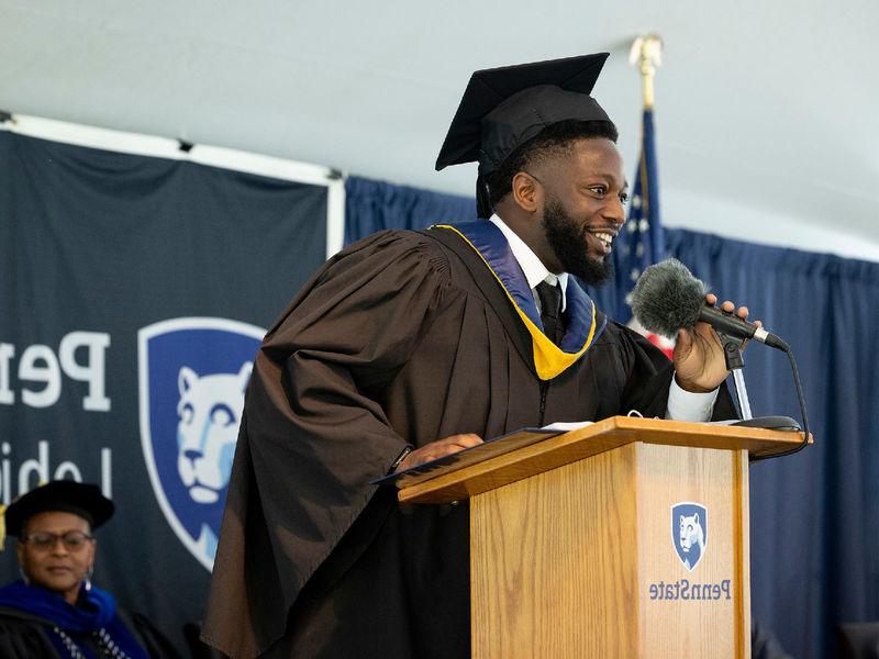 Abu Fofanah wearing commencement regalia standing at a podium speaking.